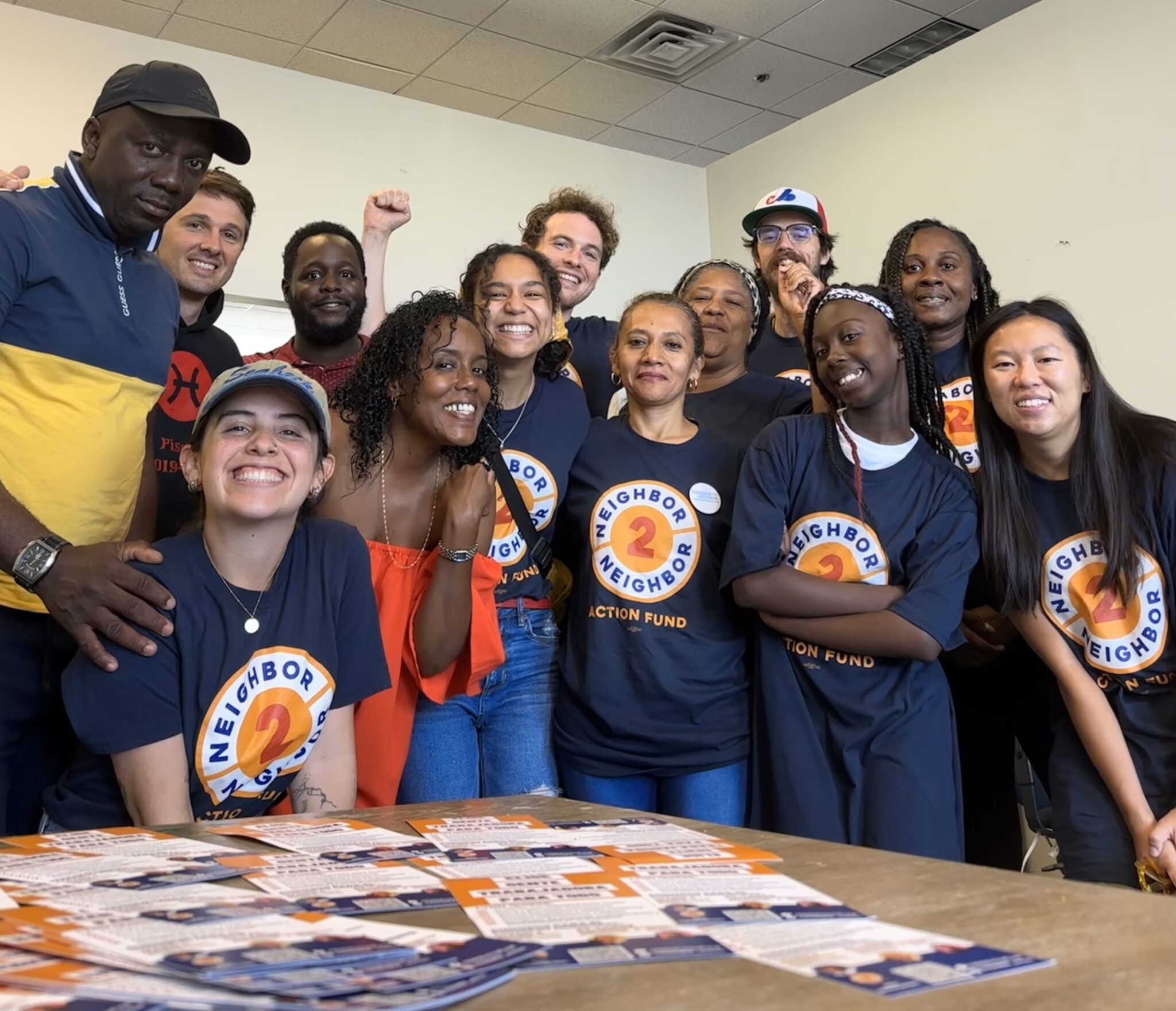 A group picture of people smiling. In the foreground, several wear a navy “Neighbor 2 Neighbor” T-shirt.